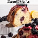 Slice of Lemon Blackberry Cake on a spatula, being held slightly above the whole bundt cake. The cake is topped with fresh juicy blackberries and a pink blackberry glaze. Text overlay reads: Lemon Blackberry Bundt Cake