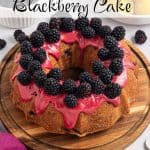 Whole Lemon Blackberry Bundt Cake on a round wooden board, topped with blackberry glaze and fresh juicy blackberries. A ramekin of fresh berries and a bowl of sliced lemons are in the background. Text overlay reads: Lemon Blackberry Cake.