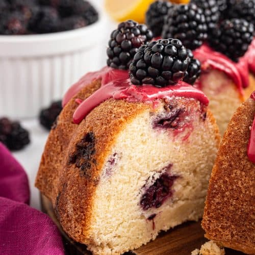 Slice of lemon blackberry bundt cake pulled away from the cake, showing moist crumb and blackberry pockets with fresh blackberries and blackberry glaze on top.