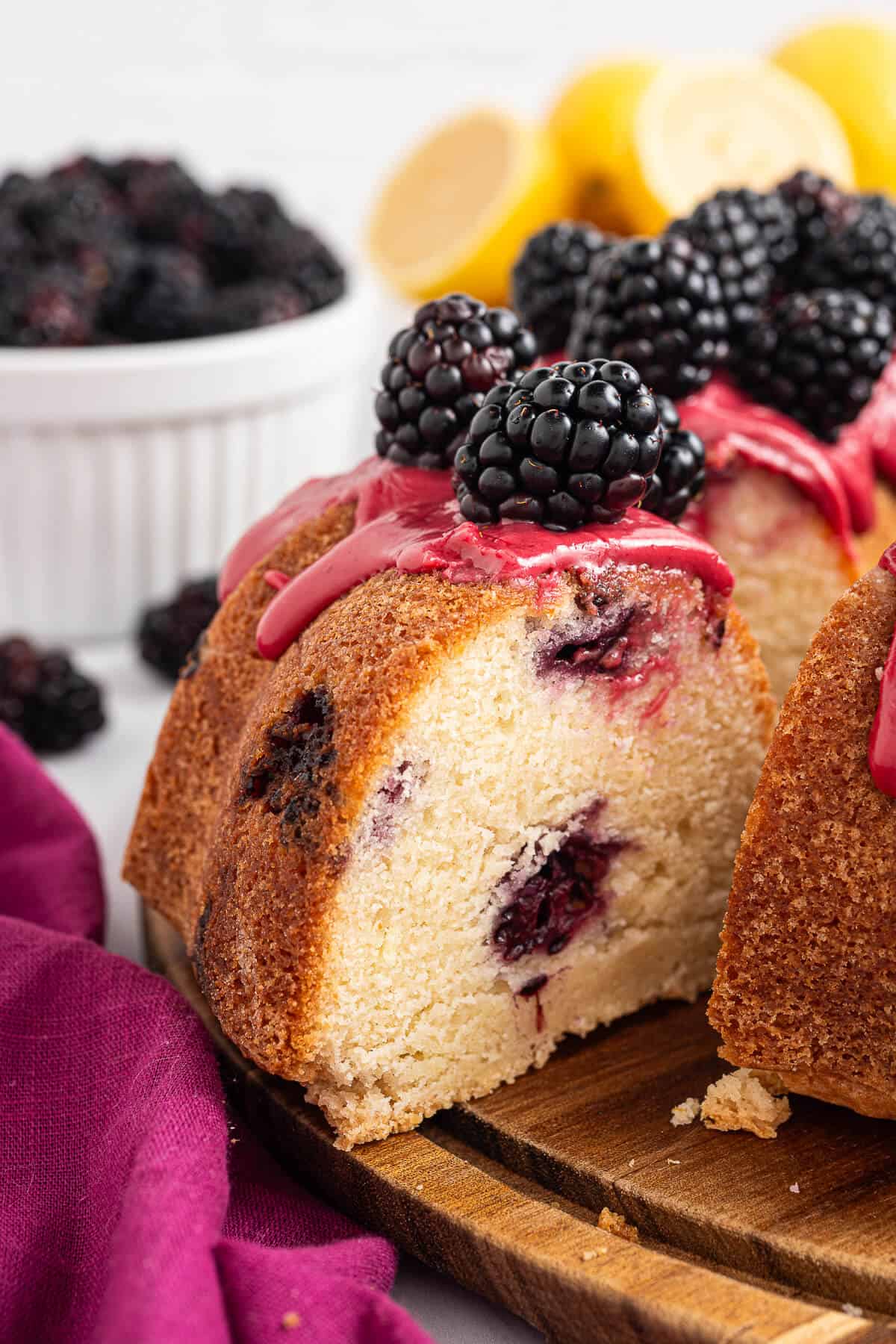 Slice of lemon blackberry bundt cake pulled away from the cake, showing moist crumb and blackberry pockets with fresh blackberries and blackberry glaze on top.