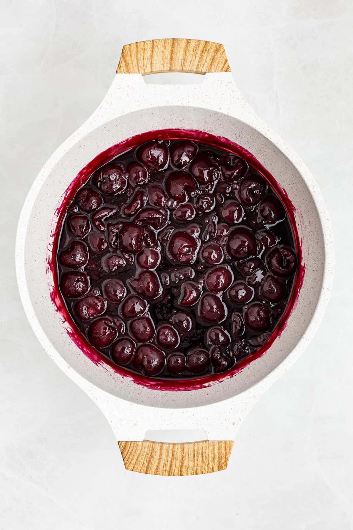 Homemade cherry compote cooking in a white pan.