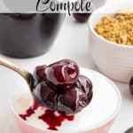 Spoon full of homemade cherry compote being placed onto a bowl full of yogurt. Granola and a jar of compote sit in the background. Text overlay reads: Cherry Compote