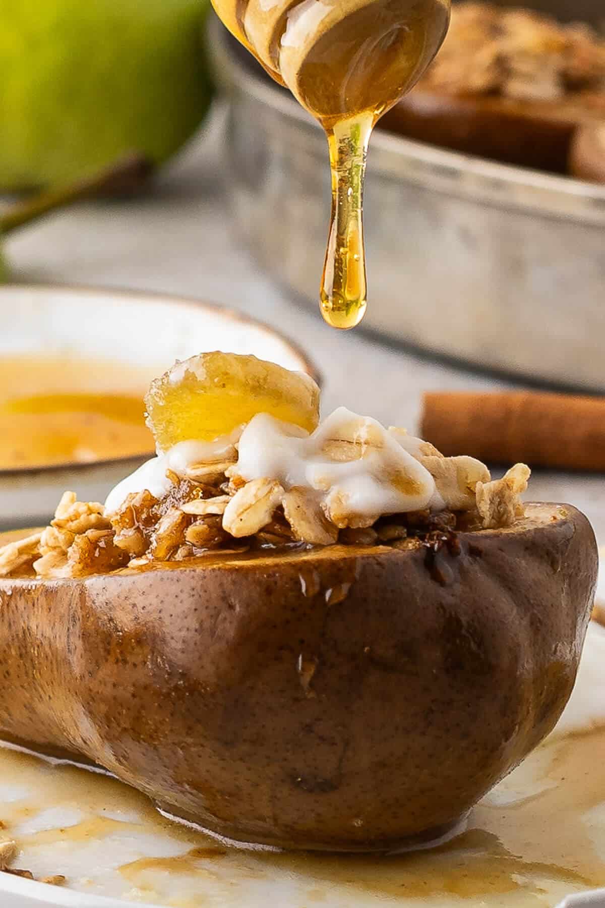 A drip of honey falling off a honey dipper and onto a baked pear half topped with oats, yogurt and candied ginger.